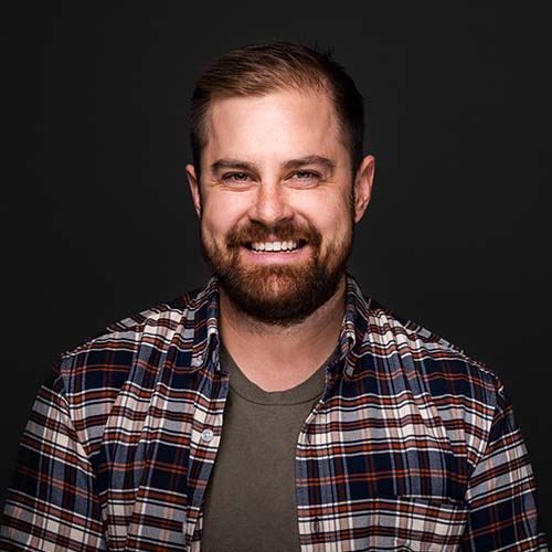 Headshot of Mitch Kuhn, a white man with green under shirt and open plaid shirt