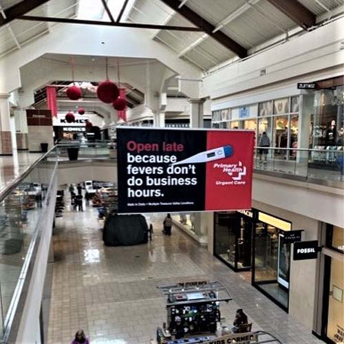 Banner hanging in mall with an image of a thermometer and text that reads "Open late because fevers don't do business hours."