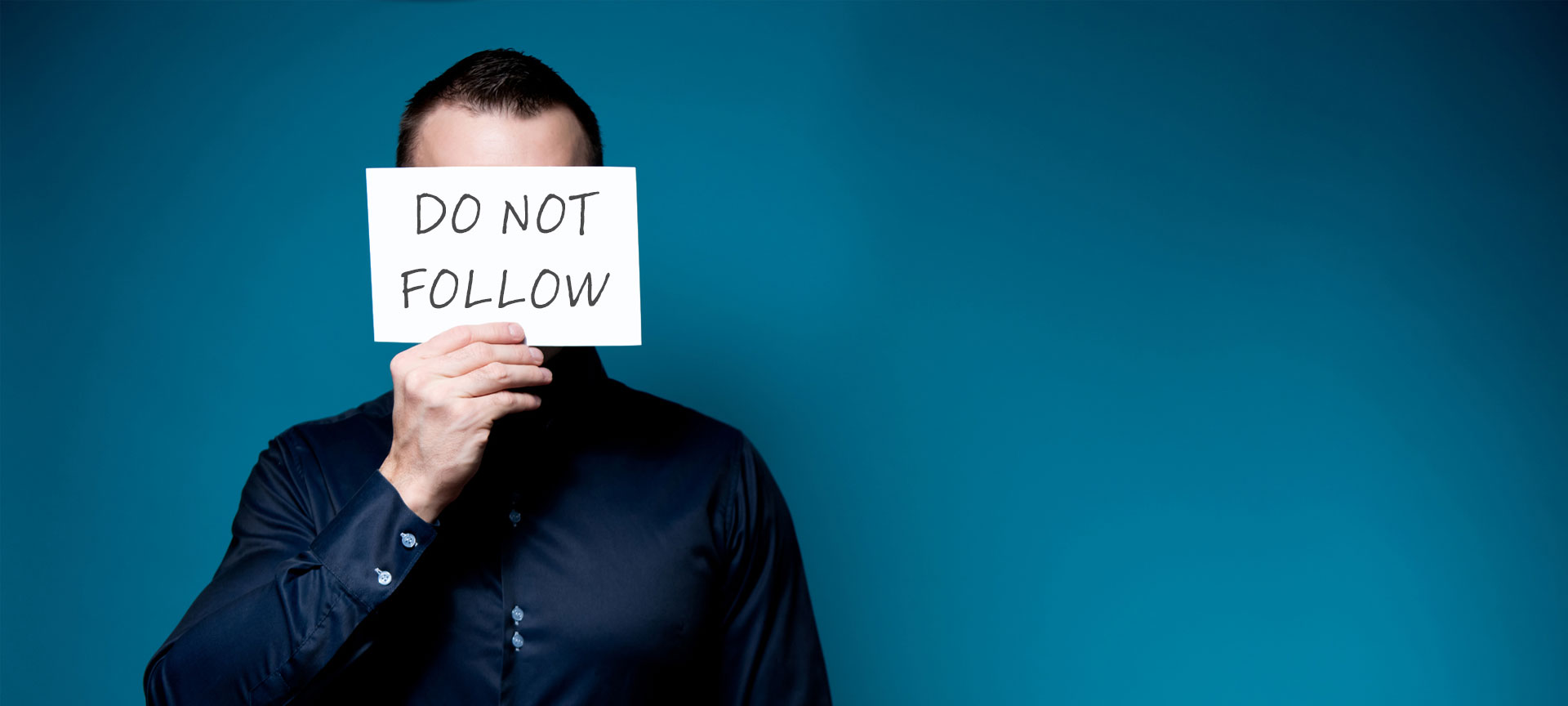 Man covering his face with a "Do Not Follow" sign