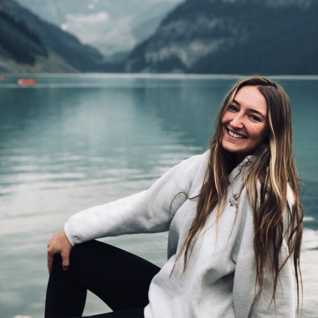 Lizzie smiling in front of a mountain lake scene