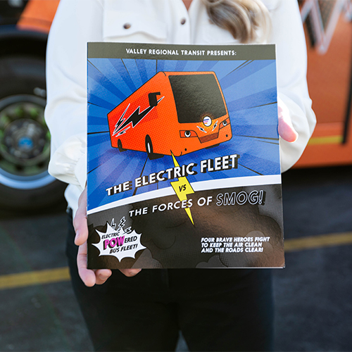 Photo of a person holding the comic book titled, "The Electric Fleet vs. The Forces of Smog".