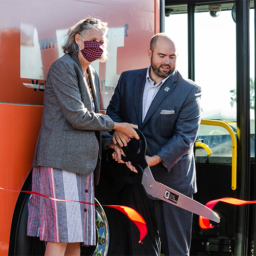 Two people cutting a ribbon in front of Valley Regional Transit's electric bus with giant scissors.