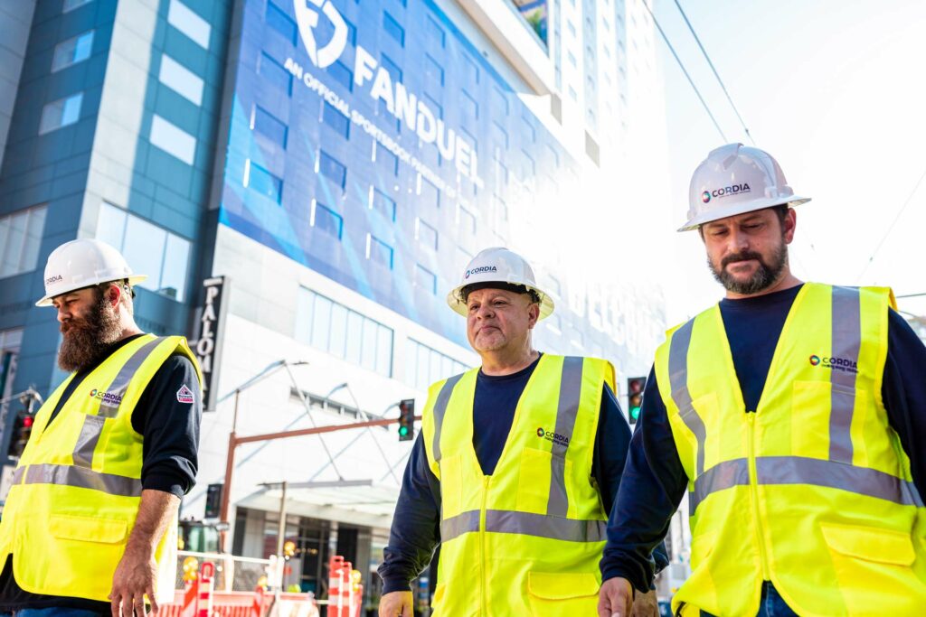 Three Cordia employees wearing safety vests and hard hats walking in front of a building.