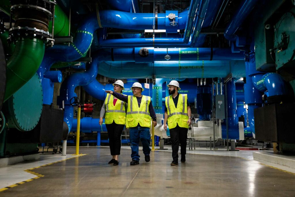 Three Cordia employees walking through a factory. The center employee is pointing something out to the other two with his hand.