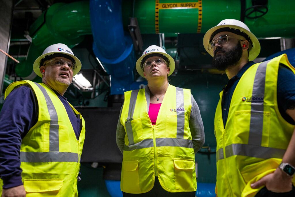 Three Cordia employees in a factory looking up at something facing the lens of the camera.