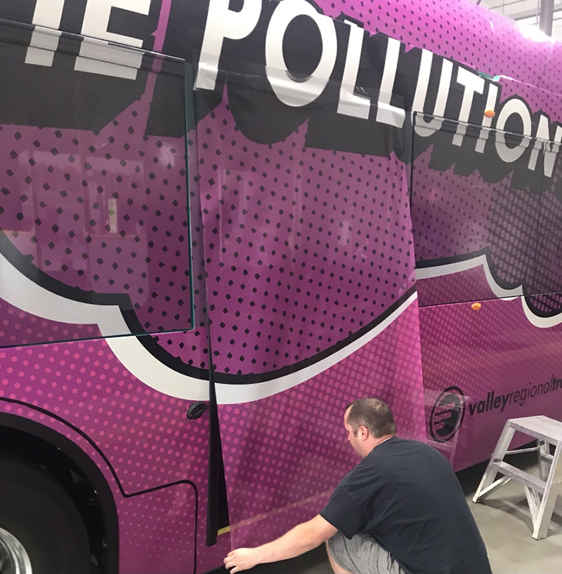 Installer placing vinyl on bold purple wrap for new electric bus