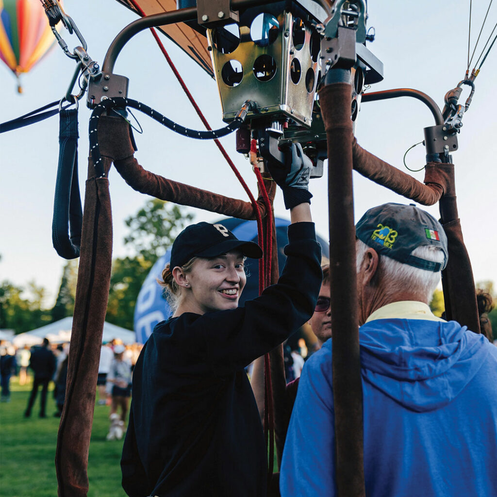 Photograph of Clara Adams smiling as she climbs into a air balloon basket